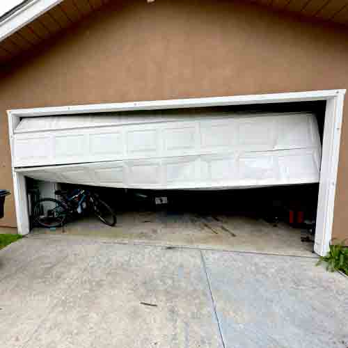 A photo showing a catastrophic garage door failure with a broken torsion spring and snapped cable, highlighting the immediate safety hazard.
