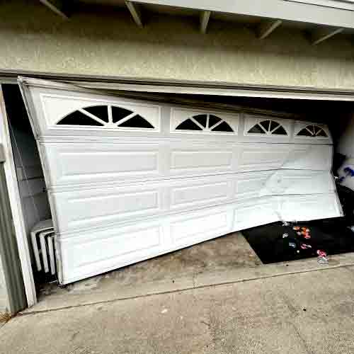 Close-up of a damaged residential garage door severely off its tracks with bent horizontal tracks, demonstrating a critical failure requiring immediate repair.