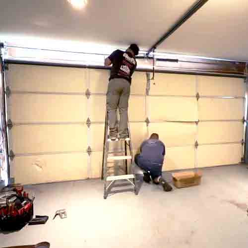 A professional technician on a ladder inspecting and fixing a garage door