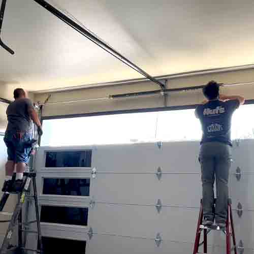 Certified technicians using professional winding bars to safely apply tension to a new replacement spring during a same-day repair appointment