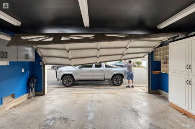 Crooked garage door stuck partly open with a technician outside