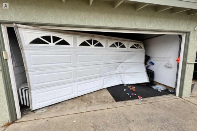 Damaged garage door hanging crooked and off track