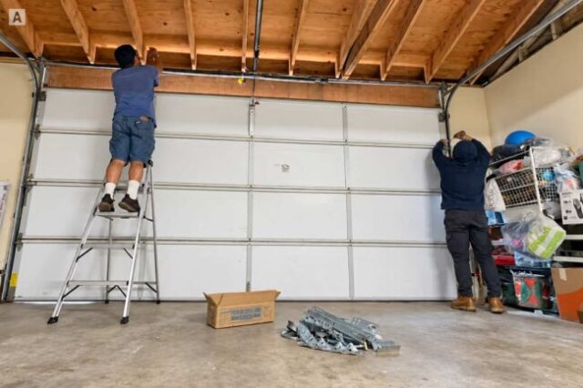 Two technicians repairing garage door track and spring inside a residential garage