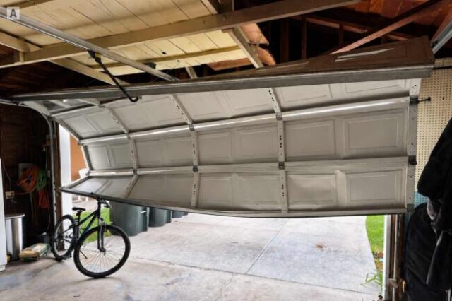 Garage door hanging unevenly off track inside a residential garage