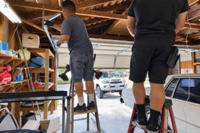Technicians repairing the track system on a garage door.