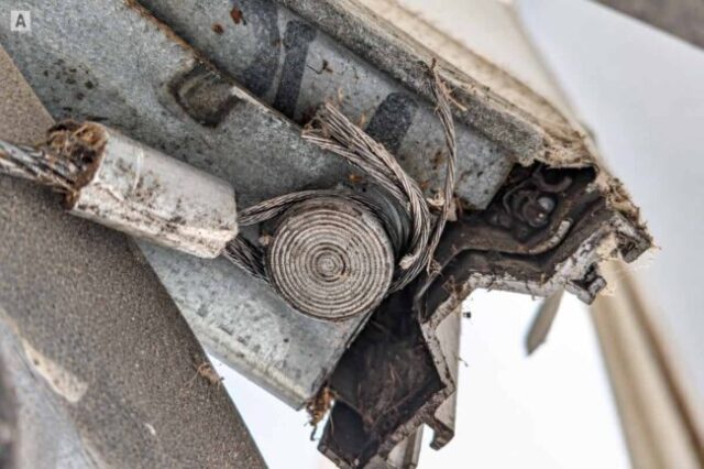 Close-up of a frayed garage door cable loop with separated steel strands near the bottom bracket.