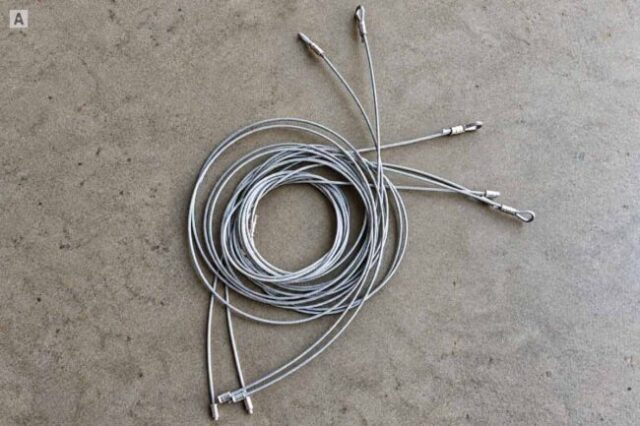 Several galvanized garage door replacement cables laid out on a concrete floor.