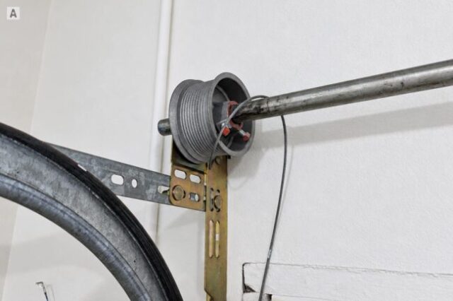 Garage door cable hanging off the drum beside the torsion shaft and spring assembly.
