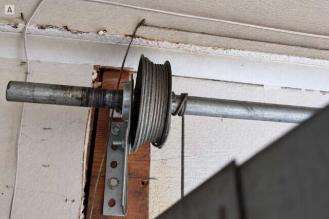Loose garage door cable wrapped around the torsion tube and cable drum.