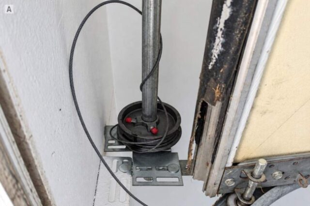 Garage door cable tangled around the drum and shaft near the top of the track.