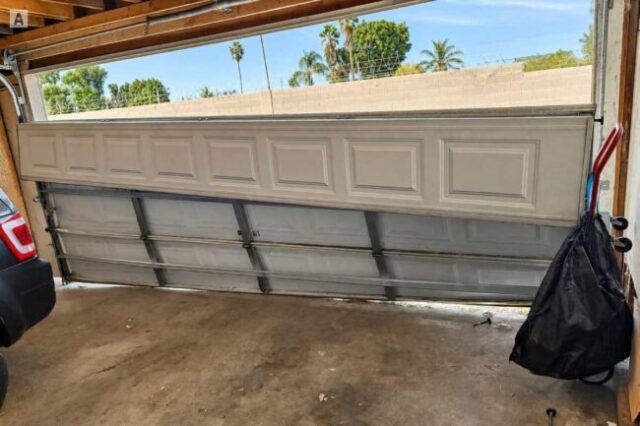 Crooked garage door sitting unevenly and off track inside a garage.